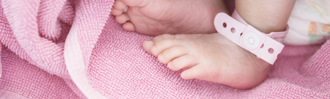 Closeup of baby feet with newborn ankle tag on bed