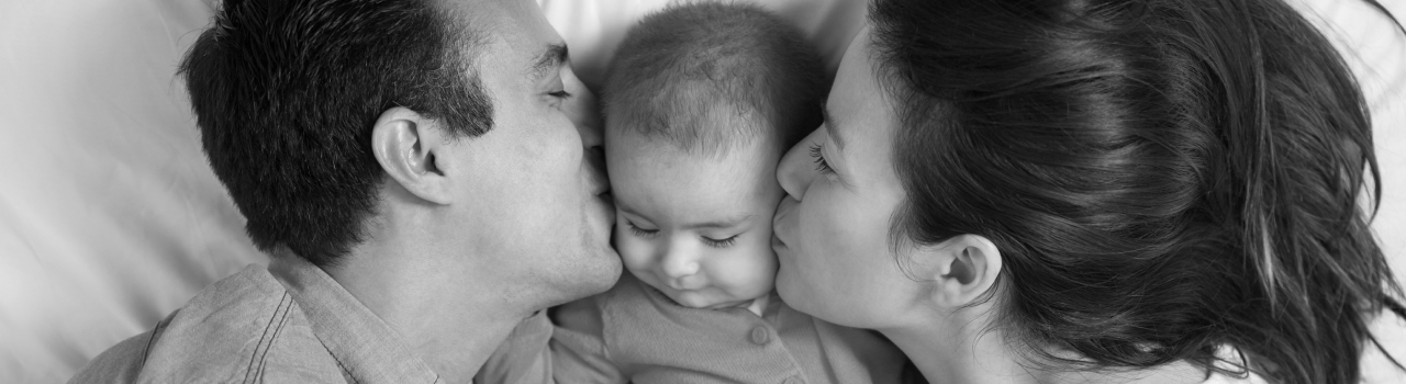 Parents kissing baby cheeks in bed