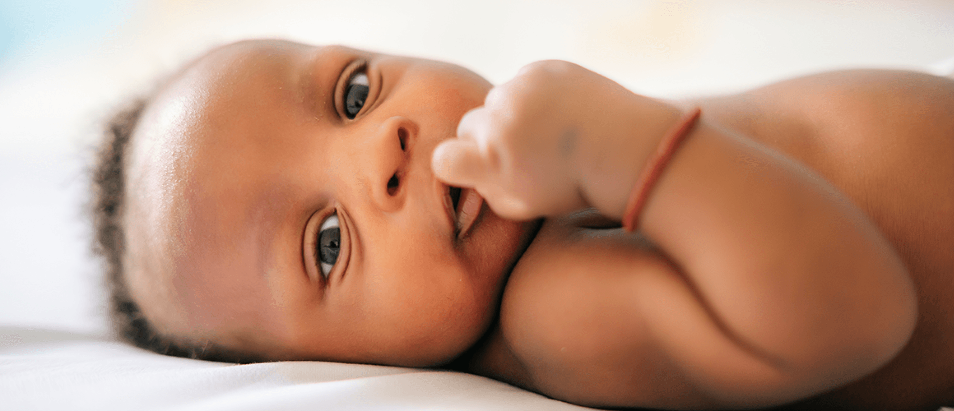 Cute baby laying on bed with finger in mouth - pregnancy and epilepsy